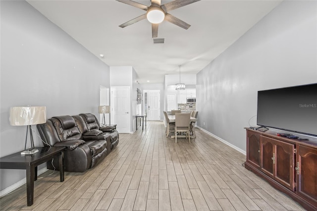 living room with ceiling fan with notable chandelier and light hardwood / wood-style floors