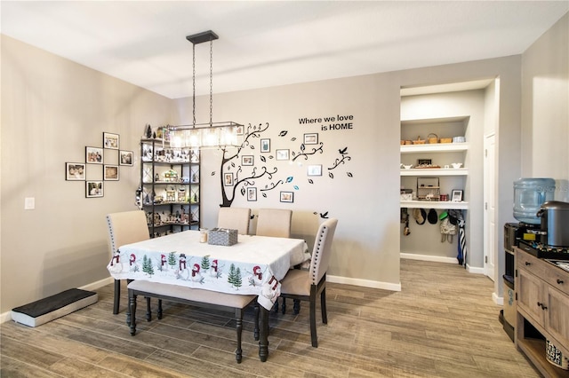 dining room featuring built in features, wood-type flooring, and an inviting chandelier