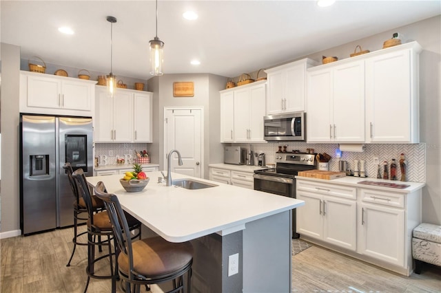 kitchen with pendant lighting, white cabinetry, stainless steel appliances, and light hardwood / wood-style flooring