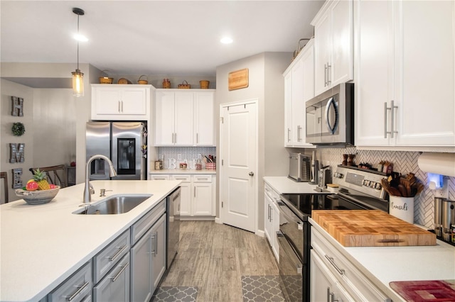 kitchen with hanging light fixtures, sink, appliances with stainless steel finishes, light hardwood / wood-style floors, and white cabinetry