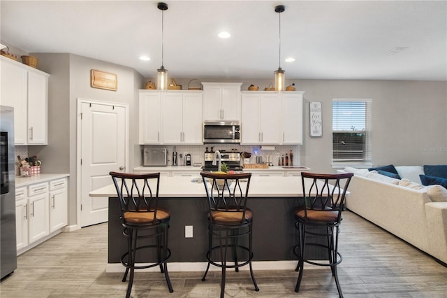 kitchen with white cabinets, pendant lighting, stainless steel appliances, and a center island with sink