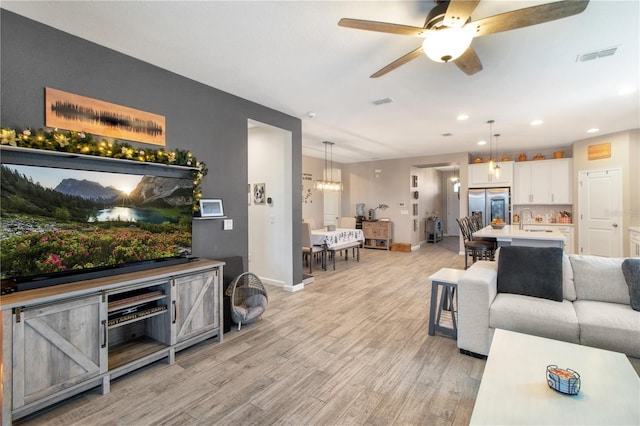 living room featuring sink, ceiling fan with notable chandelier, and light wood-type flooring