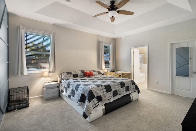 bedroom with a raised ceiling, connected bathroom, ceiling fan, and light colored carpet