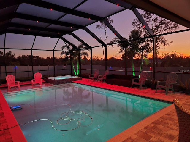 pool at dusk featuring glass enclosure, an in ground hot tub, and a patio