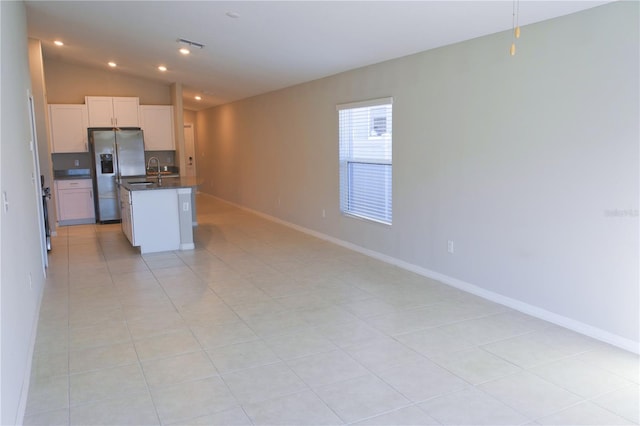 kitchen with light tile patterned floors, stainless steel fridge with ice dispenser, an island with sink, vaulted ceiling, and white cabinets