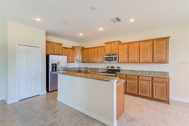 kitchen featuring stainless steel appliances, a kitchen island with sink, sink, light tile patterned floors, and stone counters