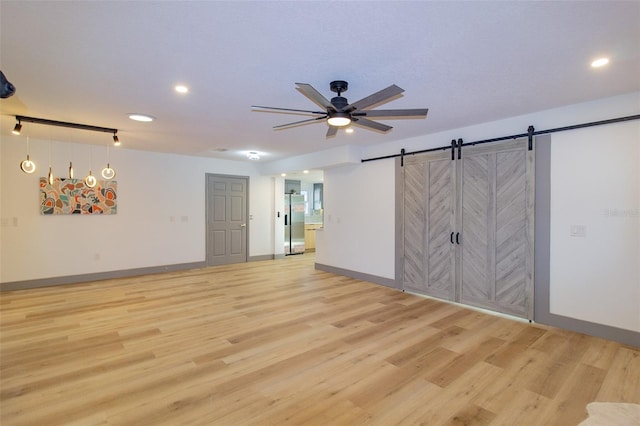 empty room with a barn door, light hardwood / wood-style floors, and ceiling fan