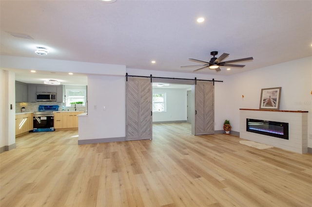 unfurnished living room featuring ceiling fan, a barn door, and light hardwood / wood-style flooring