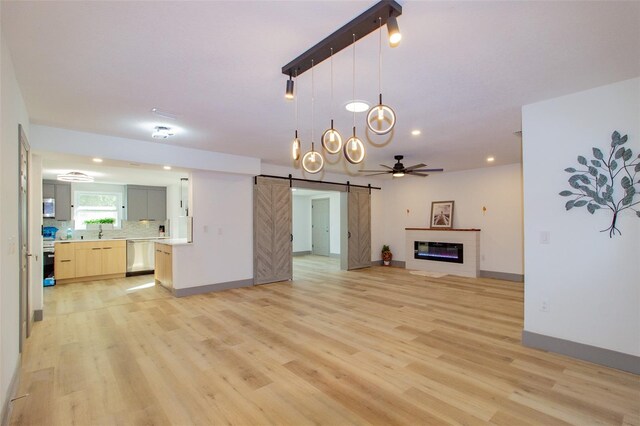 unfurnished living room featuring a barn door, light hardwood / wood-style floors, and ceiling fan