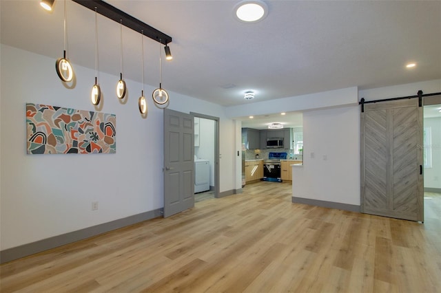 kitchen with pendant lighting, black electric range oven, a barn door, light wood-type flooring, and washer / clothes dryer