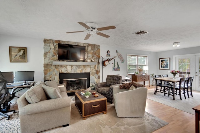 living room with ceiling fan, a fireplace, light hardwood / wood-style floors, and a textured ceiling