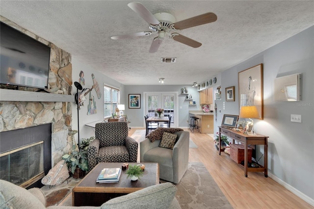 living room featuring a textured ceiling, light wood-type flooring, a stone fireplace, and ceiling fan