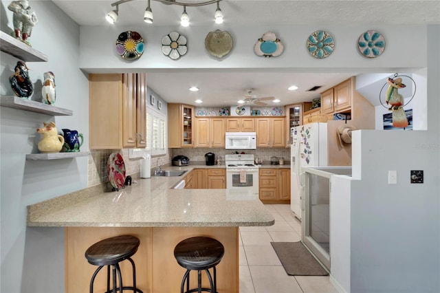 kitchen featuring a kitchen bar, kitchen peninsula, white appliances, ceiling fan, and sink