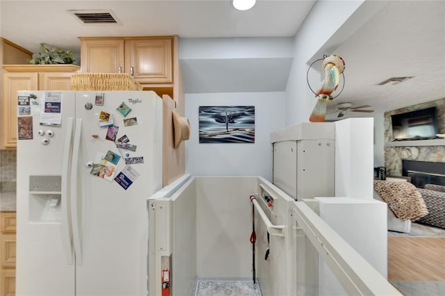 kitchen with ceiling fan, a stone fireplace, light hardwood / wood-style flooring, white refrigerator with ice dispenser, and light brown cabinetry