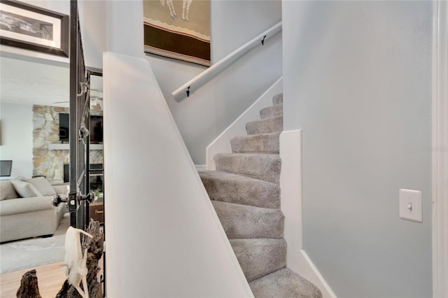 stairs with wood-type flooring and a stone fireplace