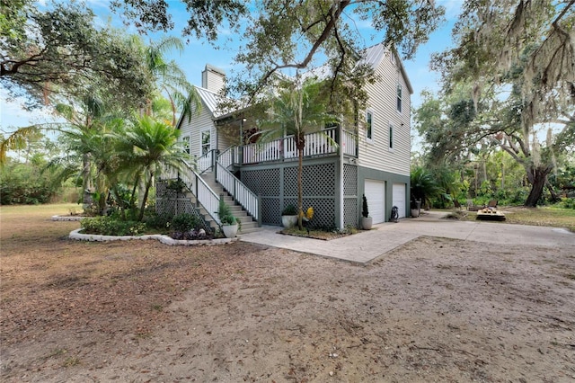 view of side of property featuring driveway, a chimney, an attached garage, stairs, and brick siding