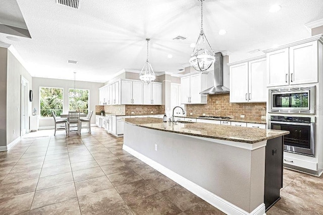 kitchen featuring stainless steel appliances, white cabinetry, a kitchen island with sink, and wall chimney range hood