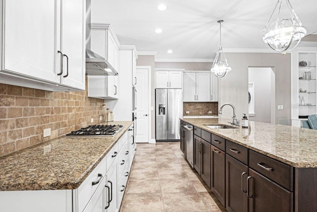 kitchen featuring appliances with stainless steel finishes, wall chimney range hood, sink, pendant lighting, and an island with sink