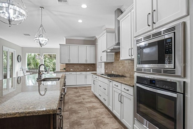 kitchen featuring a large island, sink, wall chimney range hood, decorative light fixtures, and appliances with stainless steel finishes