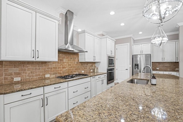 kitchen with wall chimney range hood, sink, decorative light fixtures, white cabinetry, and stainless steel appliances