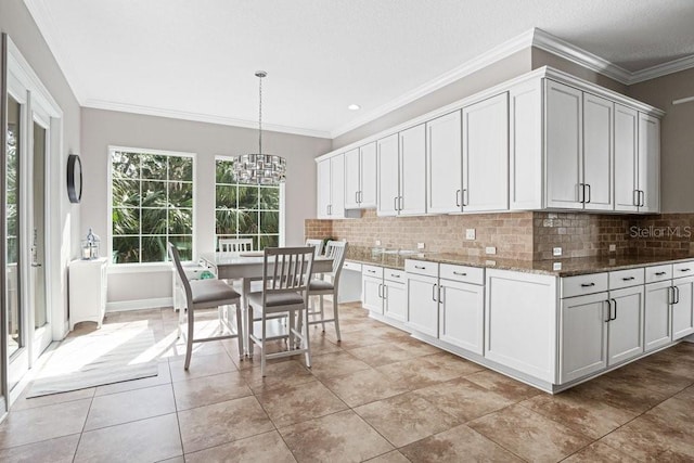 kitchen with decorative backsplash, dark stone counters, ornamental molding, pendant lighting, and white cabinets