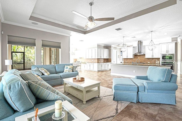 living room featuring ceiling fan, sink, a raised ceiling, crown molding, and a textured ceiling