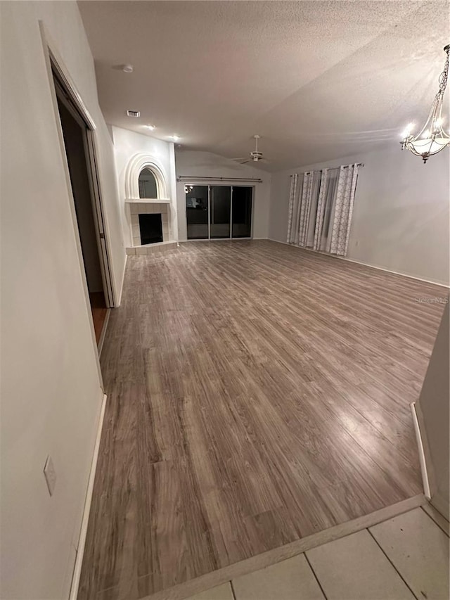 unfurnished living room with a fireplace, wood-type flooring, a textured ceiling, and ceiling fan with notable chandelier