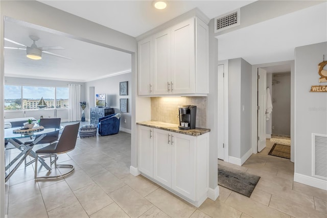 kitchen with backsplash, dark stone counters, ceiling fan, light tile patterned floors, and white cabinetry