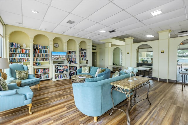 living room featuring a drop ceiling, wood-type flooring, and built in shelves