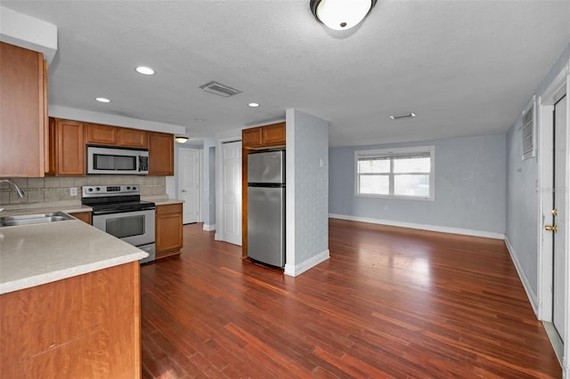 kitchen with sink, dark hardwood / wood-style flooring, a textured ceiling, decorative backsplash, and appliances with stainless steel finishes