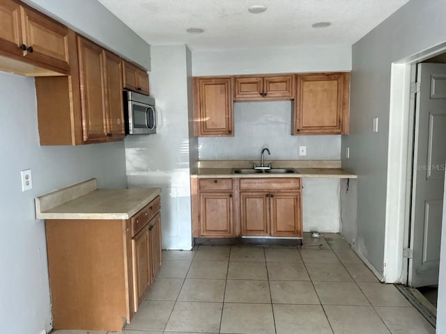 1386 19th St, Sarasota, FL 34234 - kitchen with light tile patterned floors, a sink, light countertops, stainless steel microwave, and brown cabinets