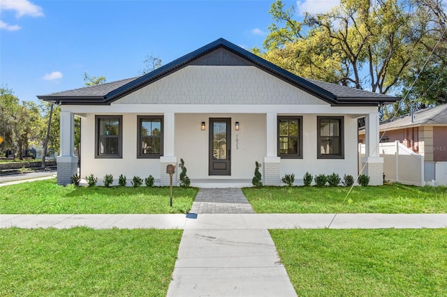 view of front of property featuring roof with shingles, covered porch, fence, a front lawn, and stucco siding