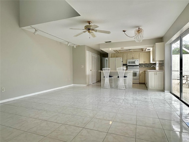 kitchen with backsplash, track lighting, white appliances, a breakfast bar area, and ceiling fan with notable chandelier