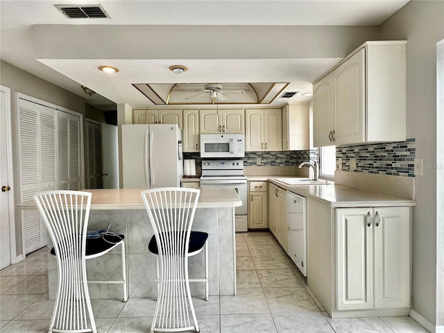 kitchen featuring ceiling fan, sink, tasteful backsplash, a kitchen breakfast bar, and white appliances