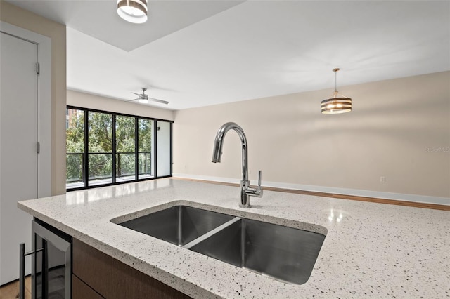 kitchen featuring light stone countertops, sink, pendant lighting, and ceiling fan with notable chandelier