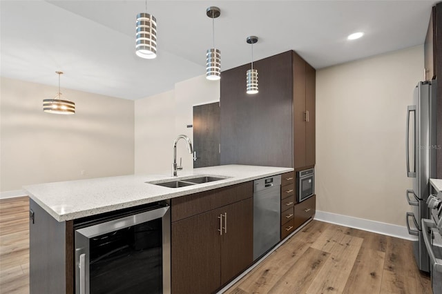 kitchen with hanging light fixtures, sink, wine cooler, light wood-type flooring, and stainless steel appliances