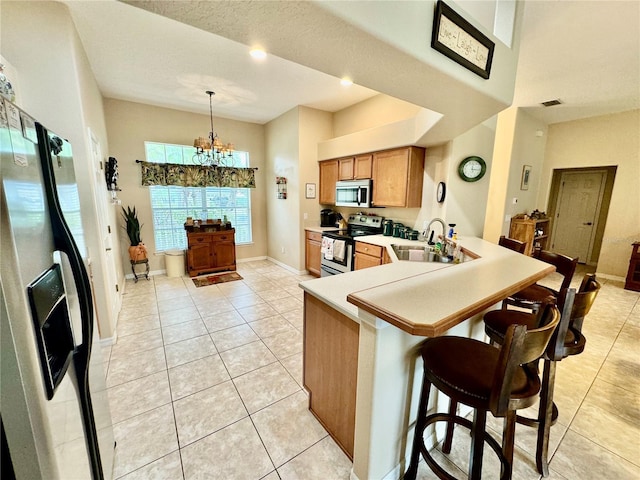 kitchen with kitchen peninsula, appliances with stainless steel finishes, sink, an inviting chandelier, and hanging light fixtures