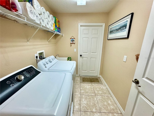 clothes washing area with washer and dryer, light tile patterned flooring, and a textured ceiling