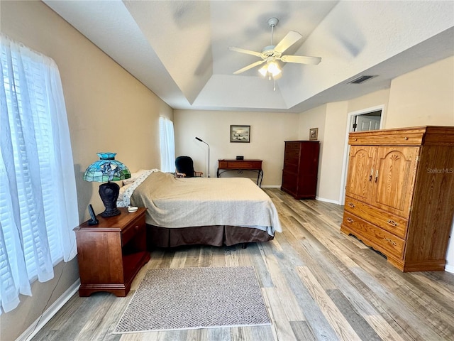 bedroom with ceiling fan, light hardwood / wood-style floors, and a tray ceiling