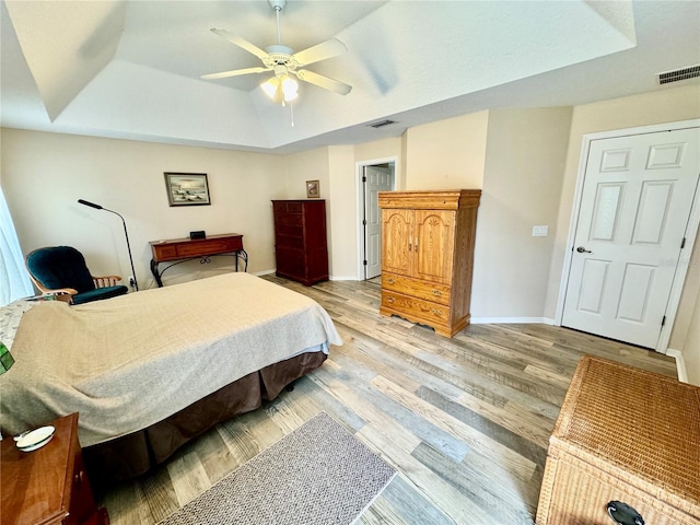 bedroom with ceiling fan, wood-type flooring, and a tray ceiling