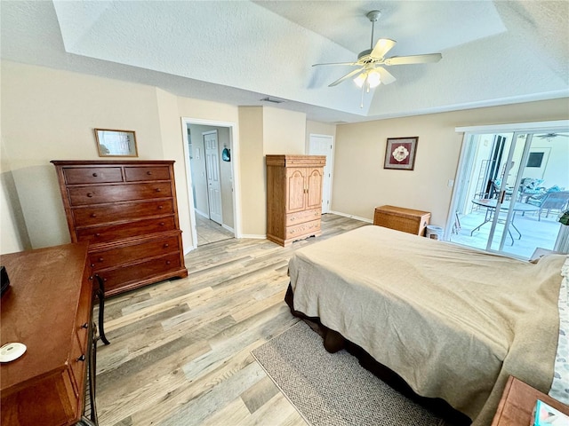 bedroom with ceiling fan, a raised ceiling, a textured ceiling, access to outside, and light wood-type flooring