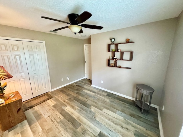 unfurnished bedroom with a closet, ceiling fan, hardwood / wood-style floors, and a textured ceiling