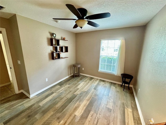 unfurnished room with ceiling fan, a textured ceiling, and light wood-type flooring