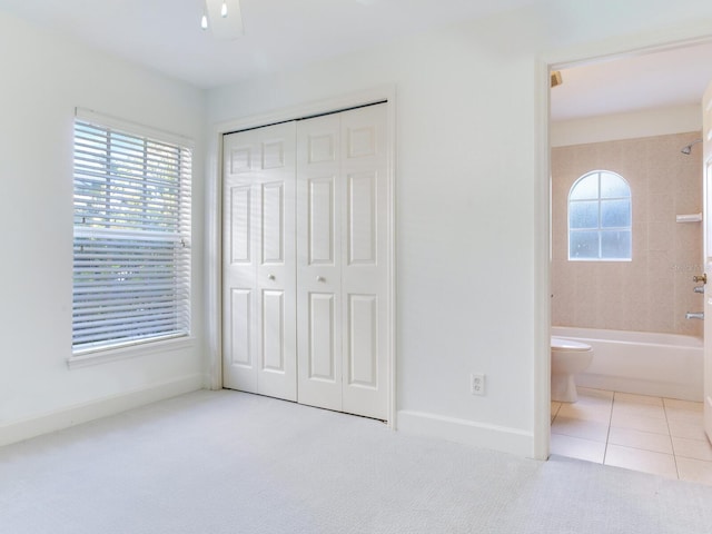 unfurnished bedroom featuring multiple windows, light carpet, a closet, and ensuite bathroom