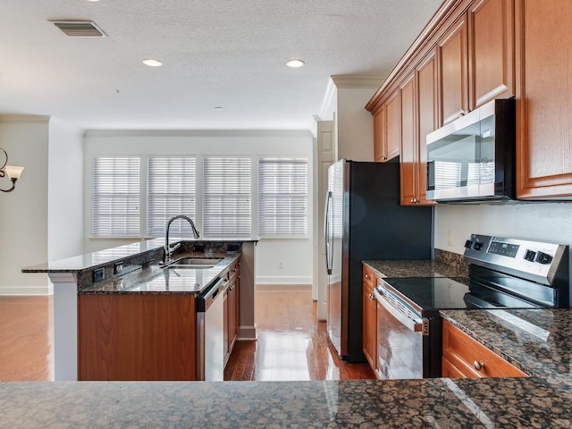 kitchen with appliances with stainless steel finishes, light wood-type flooring, ornamental molding, dark stone counters, and sink