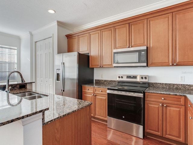 kitchen with crown molding, dark stone countertops, sink, and stainless steel appliances