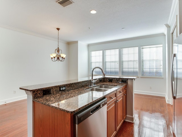 kitchen with sink, hanging light fixtures, stainless steel appliances, dark stone countertops, and light wood-type flooring