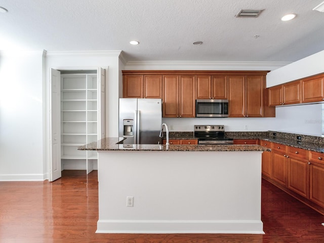 kitchen with a kitchen island with sink, dark stone counters, dark wood-type flooring, a textured ceiling, and appliances with stainless steel finishes