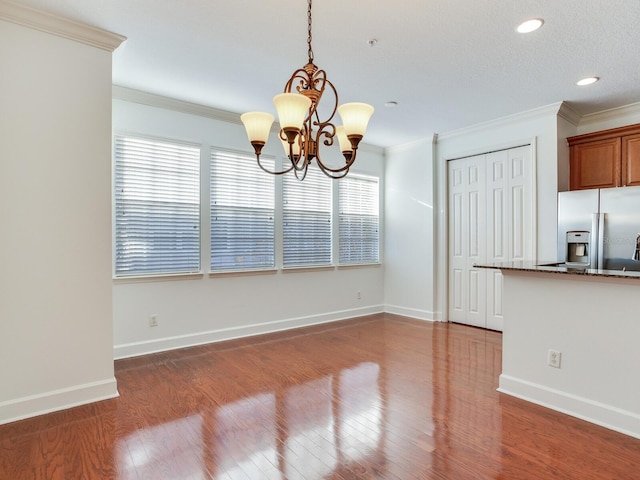 unfurnished dining area with a chandelier, dark wood-type flooring, a textured ceiling, and ornamental molding