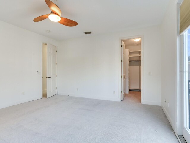 unfurnished bedroom with a spacious closet, a closet, ceiling fan, and light carpet